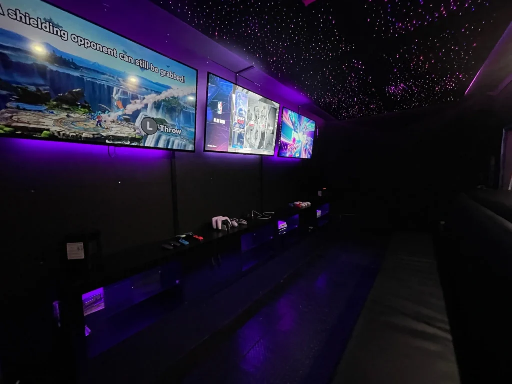 Inside the Gamers Getaway mobile gaming theatre: a row of screens, consoles and seating under purple lighting