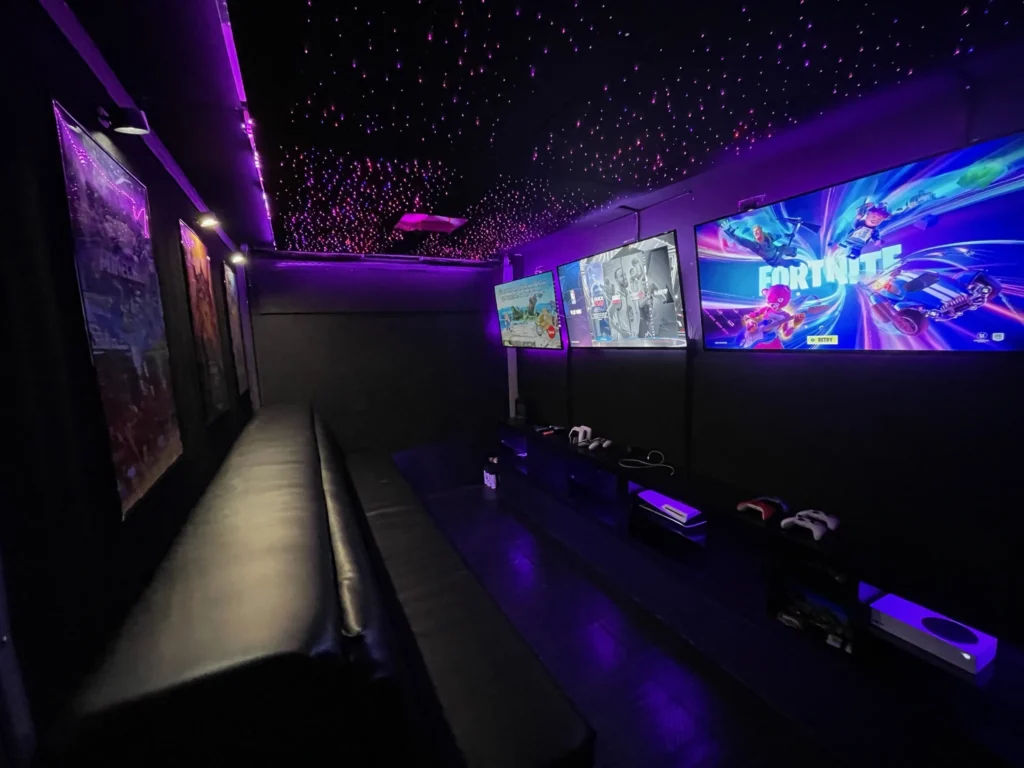 Inside a Gamers Getaway gaming trailer: one row of screens down one wall and a bench seat down the other, so a Game Coach can see every player
