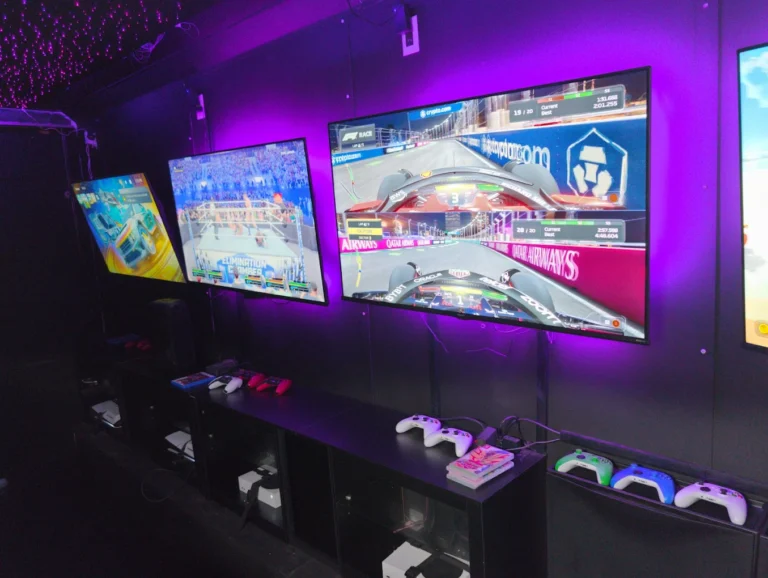 Gaming screens and controllers lined up inside the video game trailer