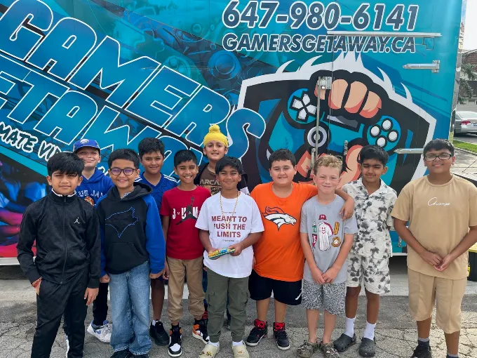 A group of kids posing in front of the Gamers Getaway video game trailer at a birthday party